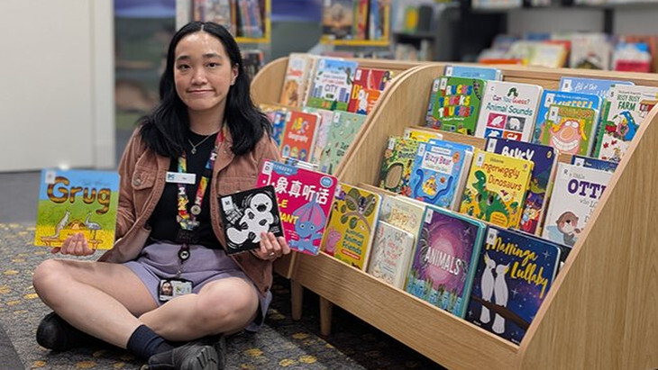 A library worker holding up three picture books at Songbirds