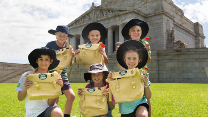 Kids on the grass outside the Shrine of Remembrance, holding kit bags and smiling