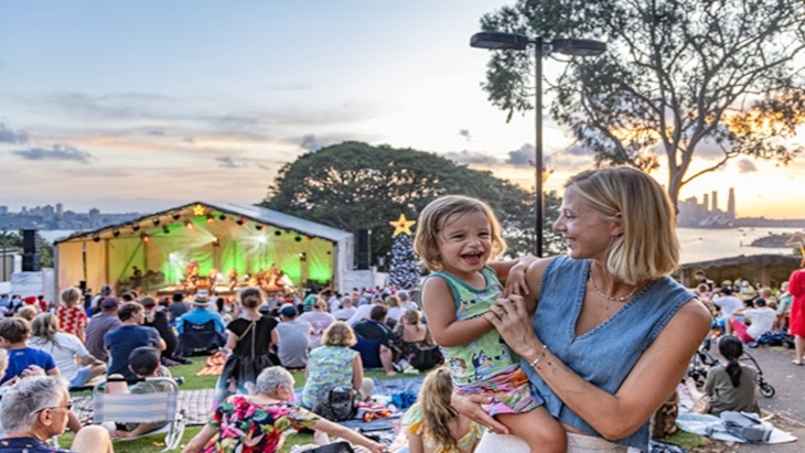 Mum holds child in arms in front of picnic and stage
