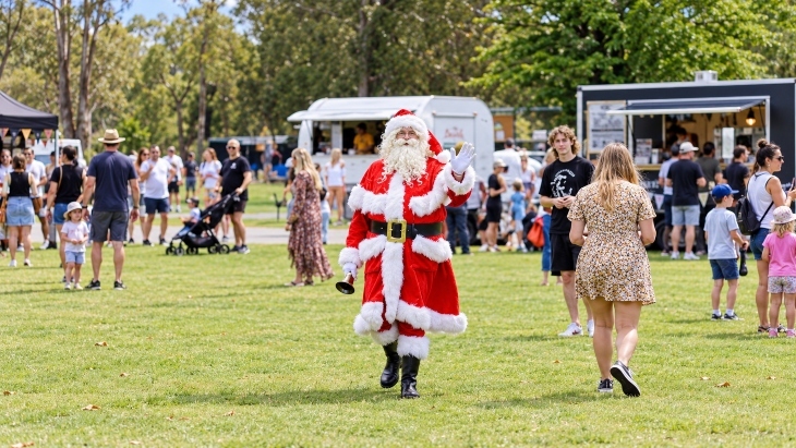 Santa waving walking through an outdoor market on grass