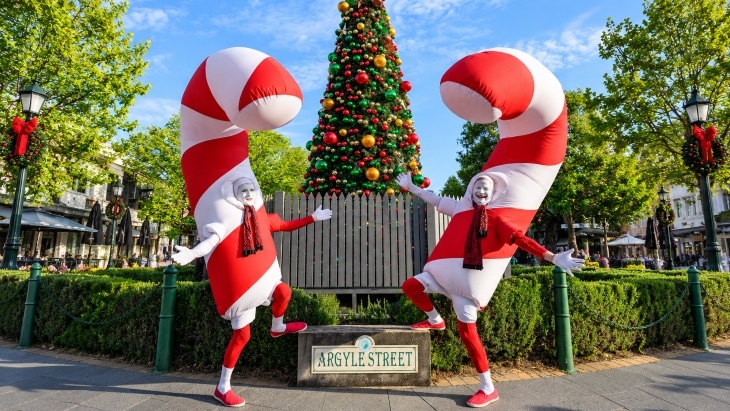Men dressed up as giant candy canes standing in front of a Christmas tree