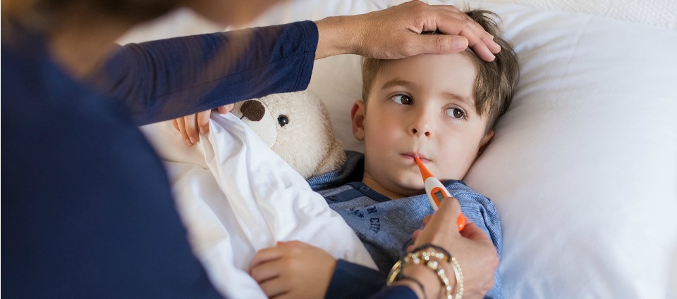 Sick boy with thermometer laying in bed and mother hand taking temperature. Mother checking temperature of her sick son who has thermometer in his mouth. Sick child with fever and illness in bed.