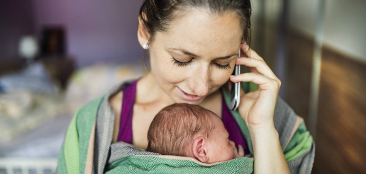 Newborn baby hold by mother in the baby wrap carrier. Mum calling at the phone. ** Note: Shallow depth of field