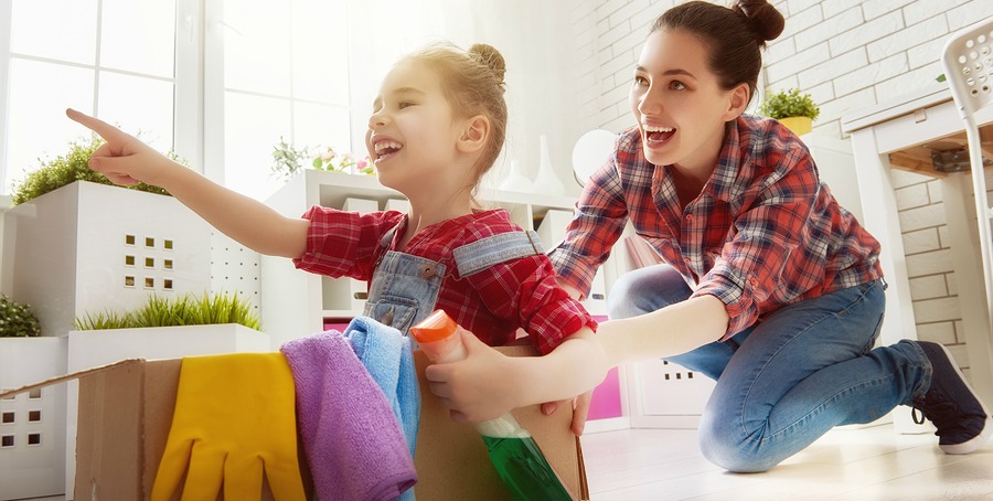 Happy family cleans the room. Mother and daughter do the cleaning in the house. A young woman and a little child girl having fun and riding in cardboard boxes at home.