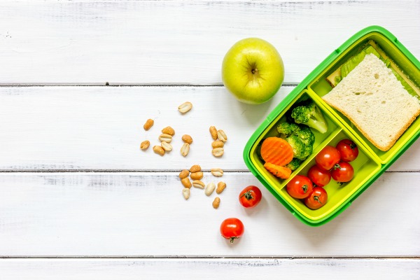 preparing lunch for child with vegetables and fruit to school top view on wooden background