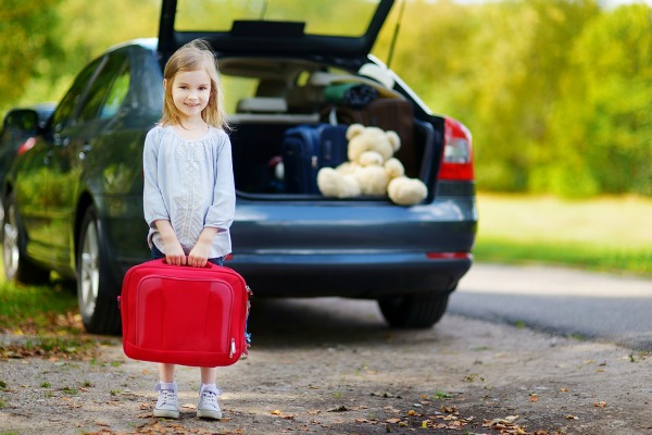Adorable little girl with a suitcase leaving for a car vacation with her parents