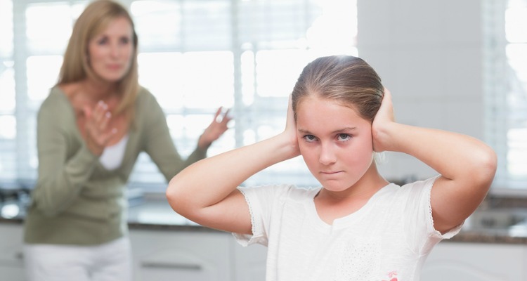 Upset little girl covering her ears while her mother screaming at home in the kitchen